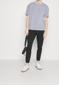 Harmaa lyhythihainen t-paita rentolla istuvuudella, yhdistetty mustiin kapealahkeisiin housuihin, valkoisiin lenkkareihin ja pieneen mustaan olkalaukkuun.