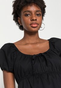 Top preto com mangas bufantes, decote franzido e detalhe com cordão. Tecido suave com textura gather, adequado para uso casual.