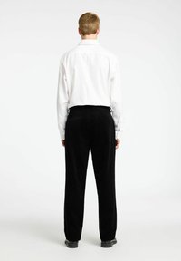 Črne kordurojske hlače s ravnim krojem in detajli pasu, v kombinaciji z belo srajco z dolgimi rokavi, prikazane s hrbtne strani.
