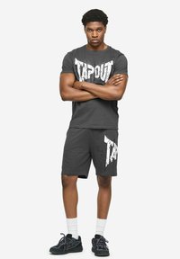 Grijs katoenen T-shirt met een witte "TAPOUT" afbeelding, gecombineerd met bijpassende shorts met een vergelijkbaar ontwerp. Draagt zwarte sneakers en witte sokken.