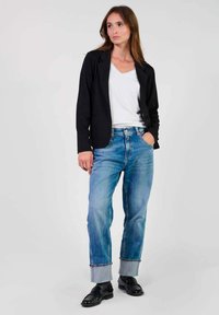 Svart blazer över en vit T-shirt med V-hals, kombinerat med ljusblå jeans med uppvikta ärmar och svarta dressade skor. Enkelt, skräddarsytt design.