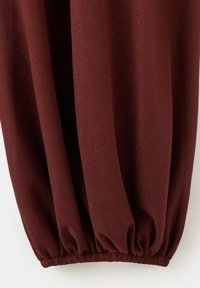 Gros plan sur une jambe de pantalon en tissu côtelé brun foncé avec un ourlet élastiqué créant des plis froncés en bas.