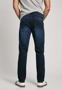 Tumed sinised teksad sirge lõikega. Omavad kahte tagataskut, millel on õrn õmbluste detail. Kandmine valgete lähetega.