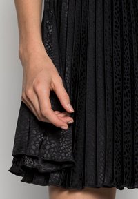 Černá plisovaná sukně s texturovaným leopardím potiskem, s vrstvenými volány na lemu a hladkým povrchem látky.