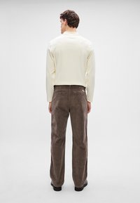 Bluză cu mânecă lungă, de culoare bej deschis, cu guler rotund; asortată cu pantaloni din catifea închisă la culoare, având buzunare la spate.