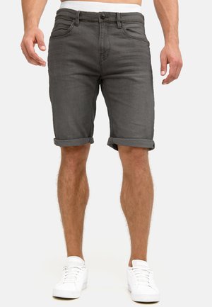 Shorts en denim gris avec ourlets roulés, cinq poches et coupe ajustée, portés avec des baskets blanches sur un fond neutre.