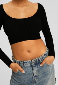 Svart ribbad långärmad crop top med rundad halsringning, kombinerad med en hög midja blek denimkjol med knappstängning och fickor.