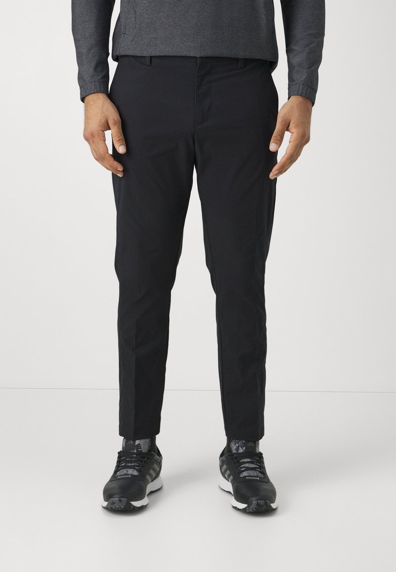 Pantaloni negri cu o croială ajustată, fabricați dintr-un material neted, asociați cu pantofi sport negri care au un design texturat și accente cu modele.