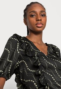 Blusa preta com decote franzido, mangas curtas bufantes e padrão de linhas onduladas com pequenas flores brancas. Tecido suave e texturizado.