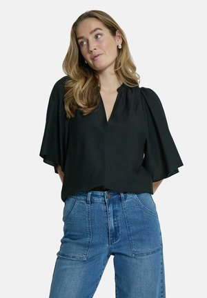 Black short-sleeve blouse with a V-neck and pleated detail, paired with high-waisted blue denim jeans featuring large pockets.