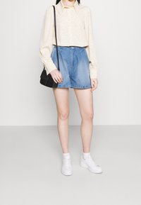 Vaaleankeltainen, pilkullinen paita pitkillä hihoilla, yhdistettynä farkkushortseihin ja valkoisiin tennareihin. Mukana musta olkalaukku.