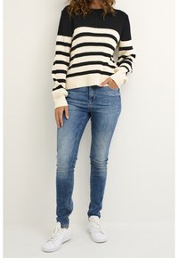 Randig stickad tröja i svart och krämfärgad; ribbad textur. Matchad med ljusblå skinny jeans och vita sneakers.