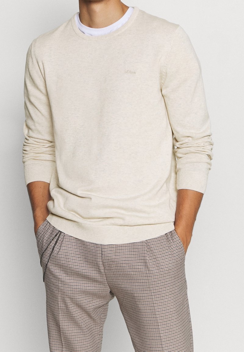 Beiger, gestrickter Pullover mit rundem Ausschnitt und gerippten Bündchen. Kombiniert mit karierten Hosen. Weiche Textur, legerer Schnitt.