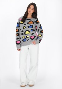 Maglione grigio a maglia con forme astratte colorate in rosa, giallo, blu e marrone. Abbinato a jeans bianchi a gamba larga e sneakers bianche.