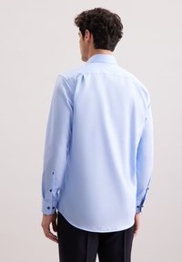 Camicia azzurro chiaro a maniche lunghe con polsini abbottonati, colletto e orlo curvo. Realizzata in tessuto liscio, presenta dettagli di design minimi.