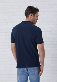 Navy polo shirt with a classic collar, short sleeves, and a straight hem, paired with light blue jeans featuring decorative stitching on pockets.