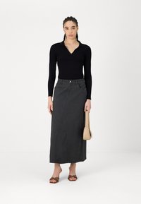Črno rebrasto dolg rokav top, v kombinaciji s sivim denim maxi krilom, ki ima žep in diagonalen šiv; model drži bež torbico.