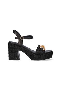 Sandalias de plataforma negras con un chunky heel texturizado, tirantes delgados en el tobillo y herrajes decorativos dorados en la parte delantera. Diseño de plantilla plana.