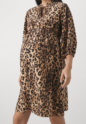 Gravid person iført knælange leopardprint kjole med trekvartærmer og bundet bælte i taljen mod hvid baggrund.