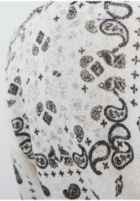 Pull en tricot blanc avec un motif paisley noir ondulant et des accents gris. Texture douce et col rond visible. L'étiquette indique le nom de la marque.
