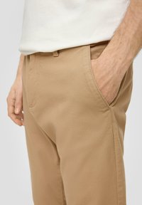Khaki spodnie z teksturowanej tkaniny, z bocznymi kieszeniami i dopasowanym krojem. Zapięcie na guzik w talii.
