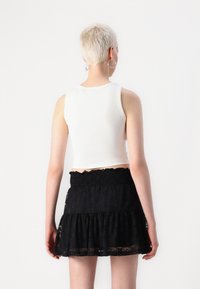 Hvit ripet crop tank top paired med et svart blonde lagdelt skjørt med elastisk midje og volangkant, sett fra baksiden.