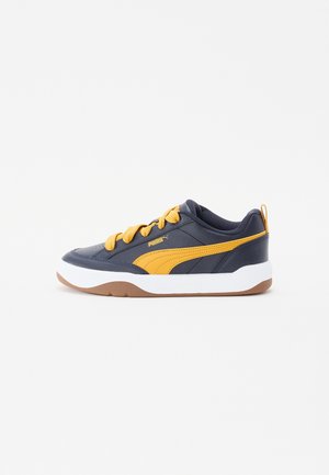 Mørkeblå sneaker med gul Puma-stribe og snørebånd, hvid mellemsål og brun ydersål, vist fra siden på hvid baggrund.
