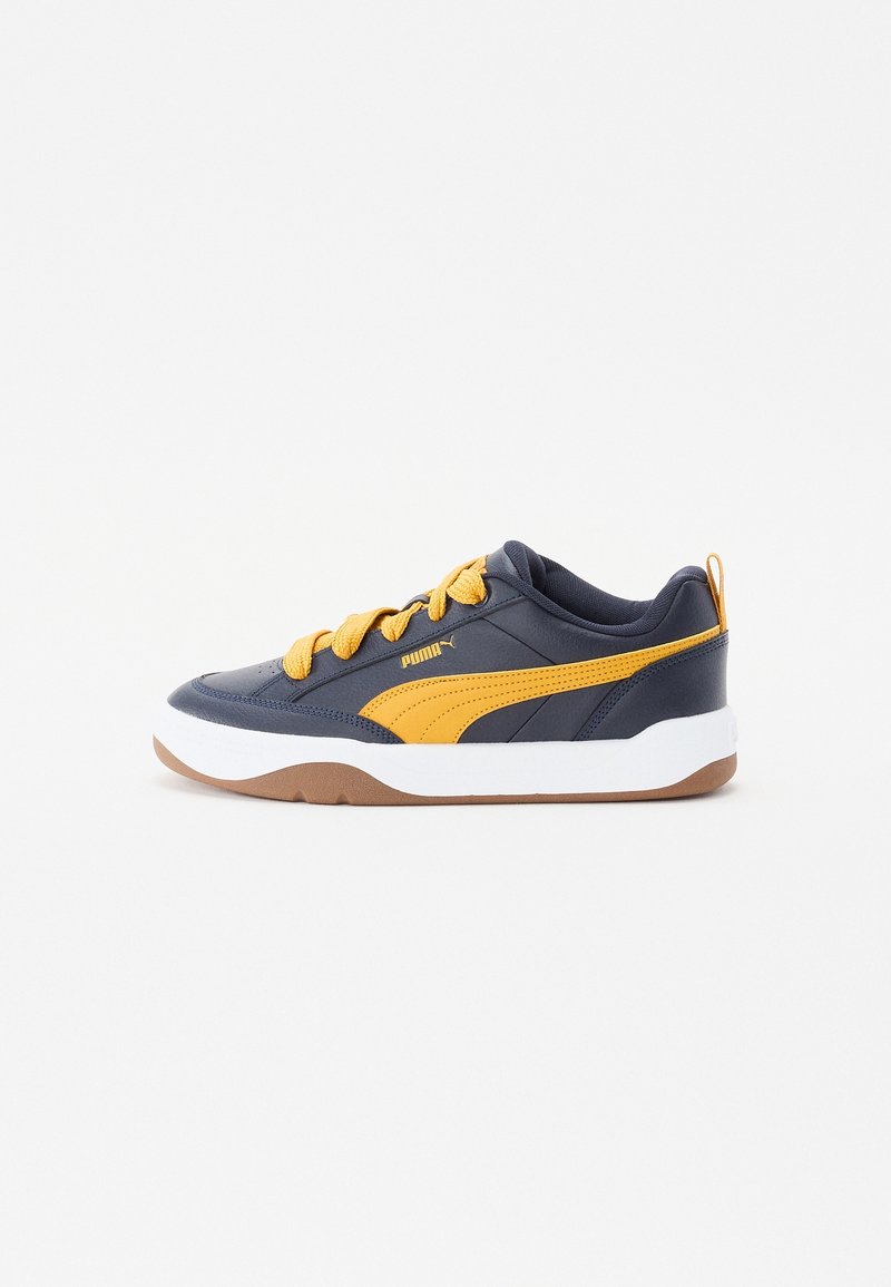 Baskets bleu marine avec bande jaune Puma et lacets, semelle intermédiaire blanche et semelle marron, vues de côté sur fond blanc.