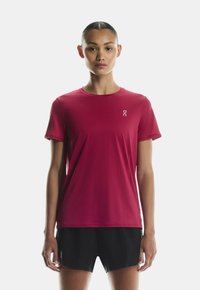 Rdeča športna majica s kratkimi rokavi in okroglim izrezom, z majhnim logotipom na levi strani prsnega koša; gladka tkanina in oprijet kroj.