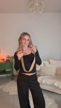 Leoprint-Gürtel mit einem beigen Riemen und runden Metallteilen, präsentiert vor einem neutralen Hintergrund mit weichen Möbeln.