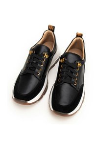 Czarne sneakersy z materiałów skórzanych i zamszowych, biała podeszwa, złote oczka i teksturowany uchwyt. Okrąły czubek z tradycyjnym sznurowaniem.