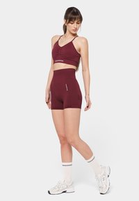 Sujetador deportivo burdeos con escote en V y sutil fruncido, combinado con pantalones cortos de talle alto que cuentan con bolsillos laterales. Tejido elástico texturizado.