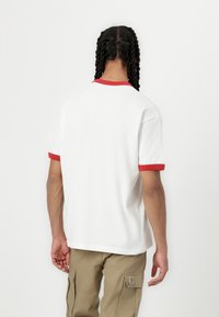 White cotton t-shirt with red ribbed neckline and sleeves, featuring a relaxed fit and straight hem, viewed from the back.