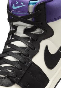 Baskets montantes avec une base en cuir blanc, accents noirs, col violet et étiquette bleue. Matériaux texturés avec lacets et coutures noirs.