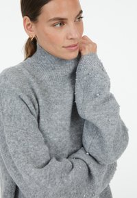 Grauer gestrickter Pullover mit hohem Rollkragen, der dezente Perlenakzente an den Ärmeln und einen weichen, strukturierten Stoff aufweist.