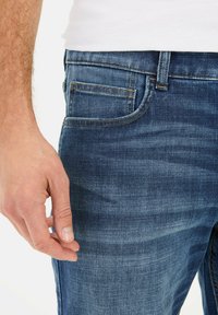 Jeans denimowe w ciemnoniebieskim kolorze o prostym kroju, z delikatnym efektownym przetarciem, pomarańczowymi szwami, kieszenią boczną i czystym wykończeniem w okolicy pasa.