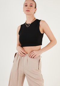 Musta lyhythihainen toppi sileästä kankaasta, yhdistettynä beigeihin löysiin housuihin, joissa on joustava vyötärö ja sivutaskut.