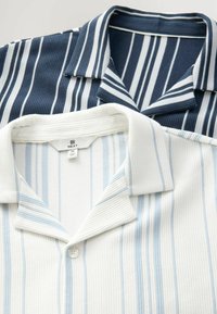 Dos camisas de cuello con rayas verticales. Una es azul marino con rayas blancas; la otra es blanca con rayas azul claro. Ambas tienen cierre de botones.