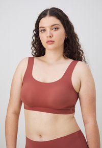 Brun, sømløs bralette med brede stropper og rund halslinning. Glatt tekstur og tettsittende design for komfort og støtte.