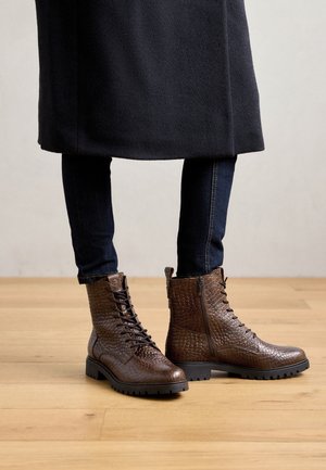 Bottes chelsea en cuir marron avec un motif texturé reptile. Elles disposent de lacets, d'une fermeture éclair latérale et d'une semelle en caoutchouc noire robuste.