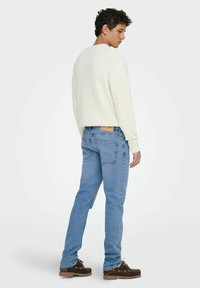 Suéter de color claro con una textura suave, combinado con jeans de denim azul. Los jeans tienen un parche trasero y bolsillos, y se llevan con zapatos oscuros.