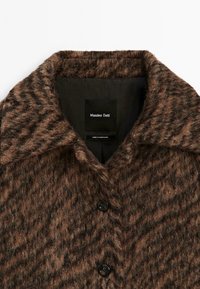 Manteau en laine texturée marron avec large col et deux boutons noirs, affichant l'étiquette de la marque Massimo Dutti à l'intérieur du col.