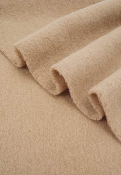 Beige filt stof med en blød, struktureret overflade, der har synlige rullekanter og overlappende folder, hvilket skaber et lagdelt udseende.