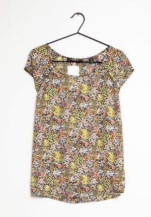 Blouse à manches courtes avec motif floral multicolore en jaune, orange, vert, bleu et noir, présentée sur un cintre noir sur fond blanc.