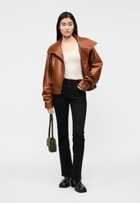 Brun läderjacka med stor krage, dragkedja och veckade ärmar. Bärs med en figursydd topp, svarta utsvängda jeans och svarta skor.