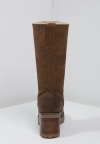 Botte en cuir marron jusqu'au genou avec une finition texturée, une pointe arrondie et un large talon en bois à motif. Doublure en fausse fourrure en haut.