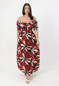 Maxikjole med off-shoulder ærmer, rød og beige blomstret mønster på sort baggrund, smocket talje og flydende stofstruktur.