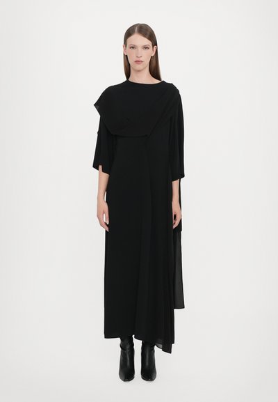 Black long dress with asymmetric draped design and wide sleeves, crafted from lightweight fabric. Paired with knee-high black boots.