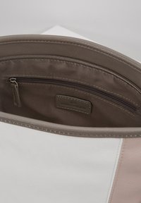 Interno della borsa in pelle color sabbia e rosa chiaro; presenta una tasca con zip e una fodera color sabbia; l'esterno include un pannello beige chiaro e un'etichetta con logo.
