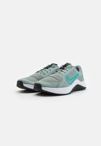 Par de zapatillas de correr Nike gris-verdosas con suelas negras, logotipos Swoosh en aguamarina, parte superior de malla y mediasuelas blancas, exhibidas sobre fondo blanco.